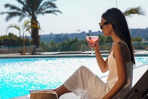 A person sitting by a pool with a drink, palm trees, and a clear sky. - Holiday Inn Cairo Maadi by IHG (Cairo)