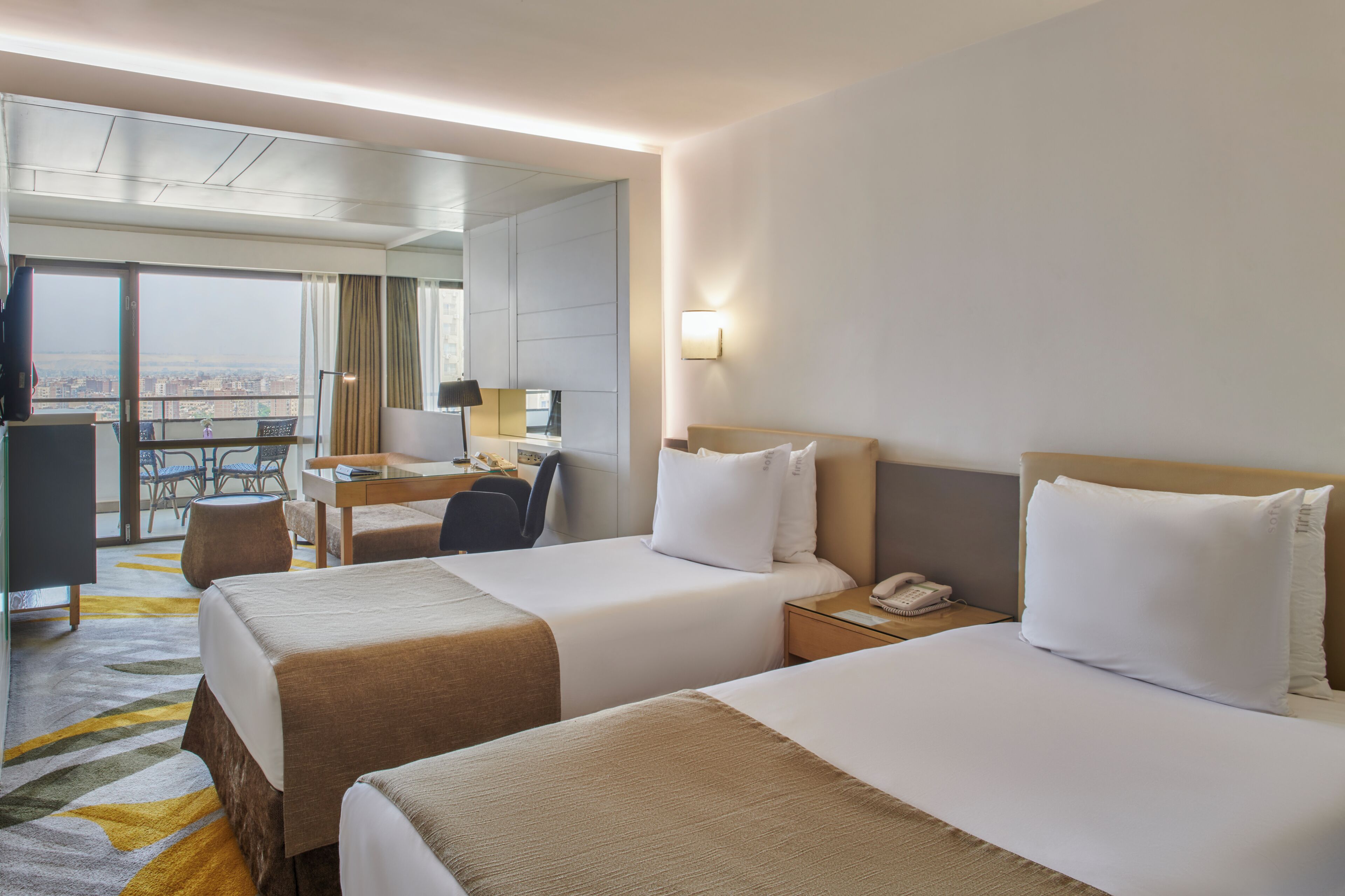 A hotel room with two beds, a desk, a chair, a phone, and a view of the city.