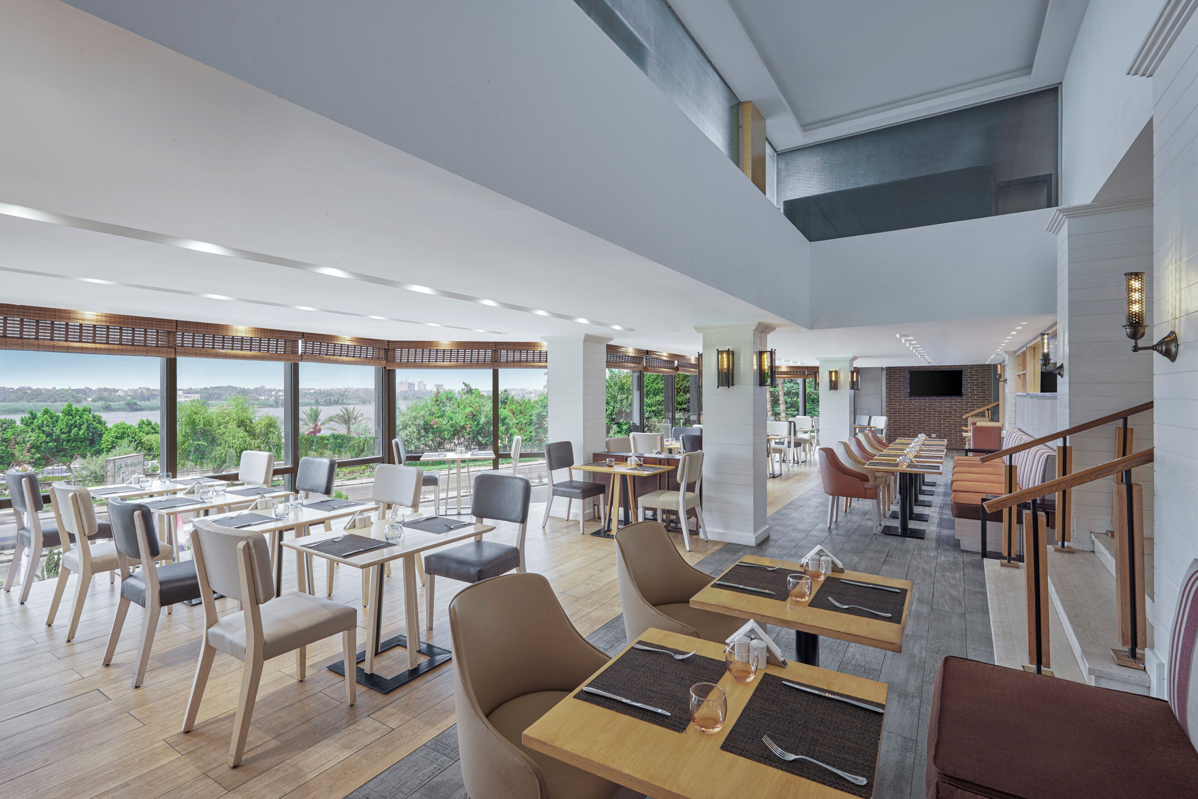 Un restaurante espacioso con techos altos, amplias ventanas y vistas a la ciudad.