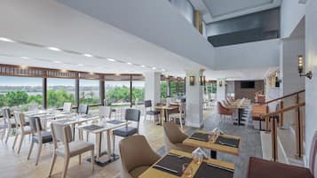 A spacious restaurant with high ceilings, large windows, and a view of the cityscape.