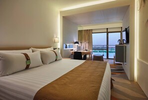 Quarto de hotel com uma cama grande, uma escrivaninha com cadeira, televisão e vista para o exterior.