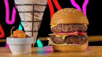 A burger with lettuce, tomato, and cheese, and a small bowl of fries on a wooden table.