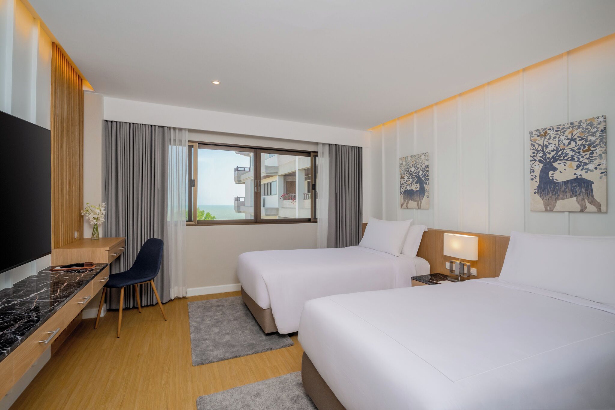 Ein Hotelzimmer mit zwei Betten, einem Schreibtisch, einem Stuhl, einem Fernseher und einem Fenster mit Vorhängen.