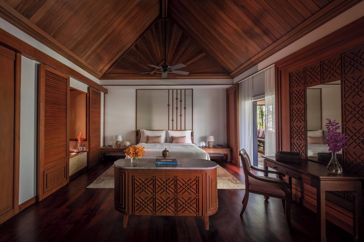 Een slaapkamer met een houten plafond, een bed, een bureau en een stoel.