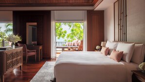 Une chambre spacieuse avec un grand lit, un bureau et une chaise. Elle dispose d’un balcon avec vue sur les palmiers.