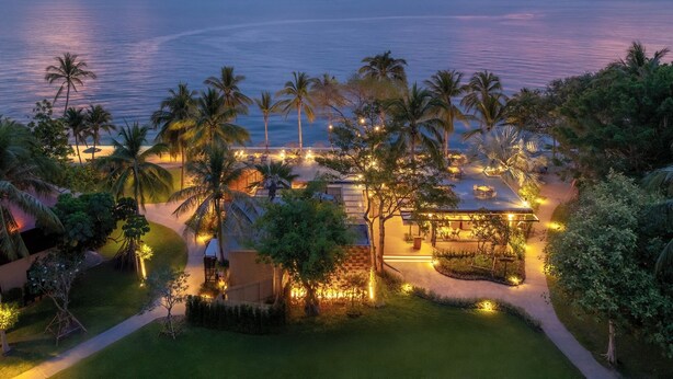 A resort with a beach view, palm trees, and outdoor seating areas.