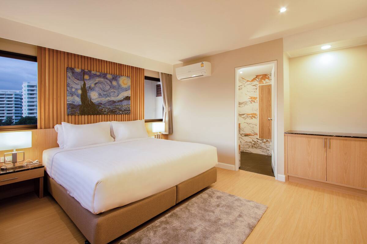Een moderne hotelkamer met een groot bed, houten lambrisering, een airconditioningapparaat, een schilderij aan de muur en uitzicht over de stad.