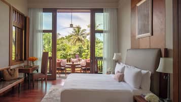 Habitación de hotel con una cama grande, un escritorio con una silla, una mesita con otra silla, y vistas a un jardín exuberante a través de una puerta corrediza.