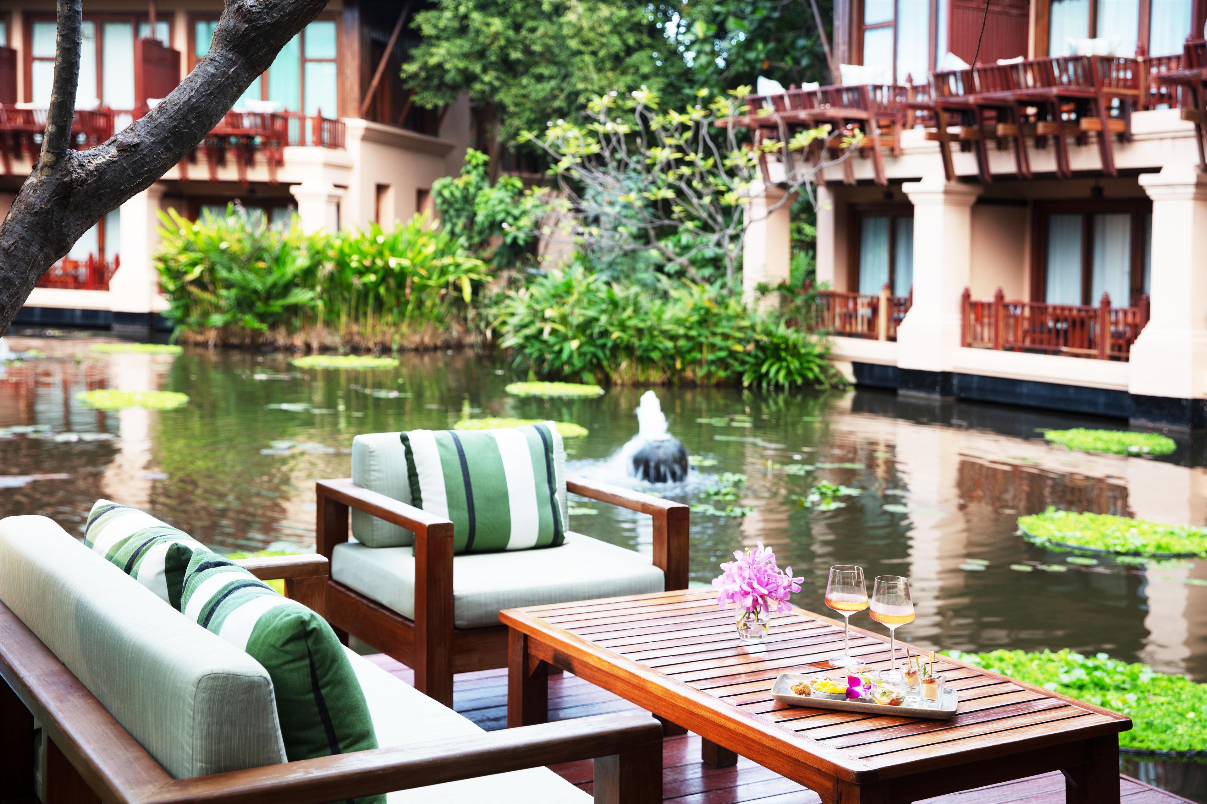 A serene outdoor seating area with a wooden table, chairs, and a view of a pond with lily pads.