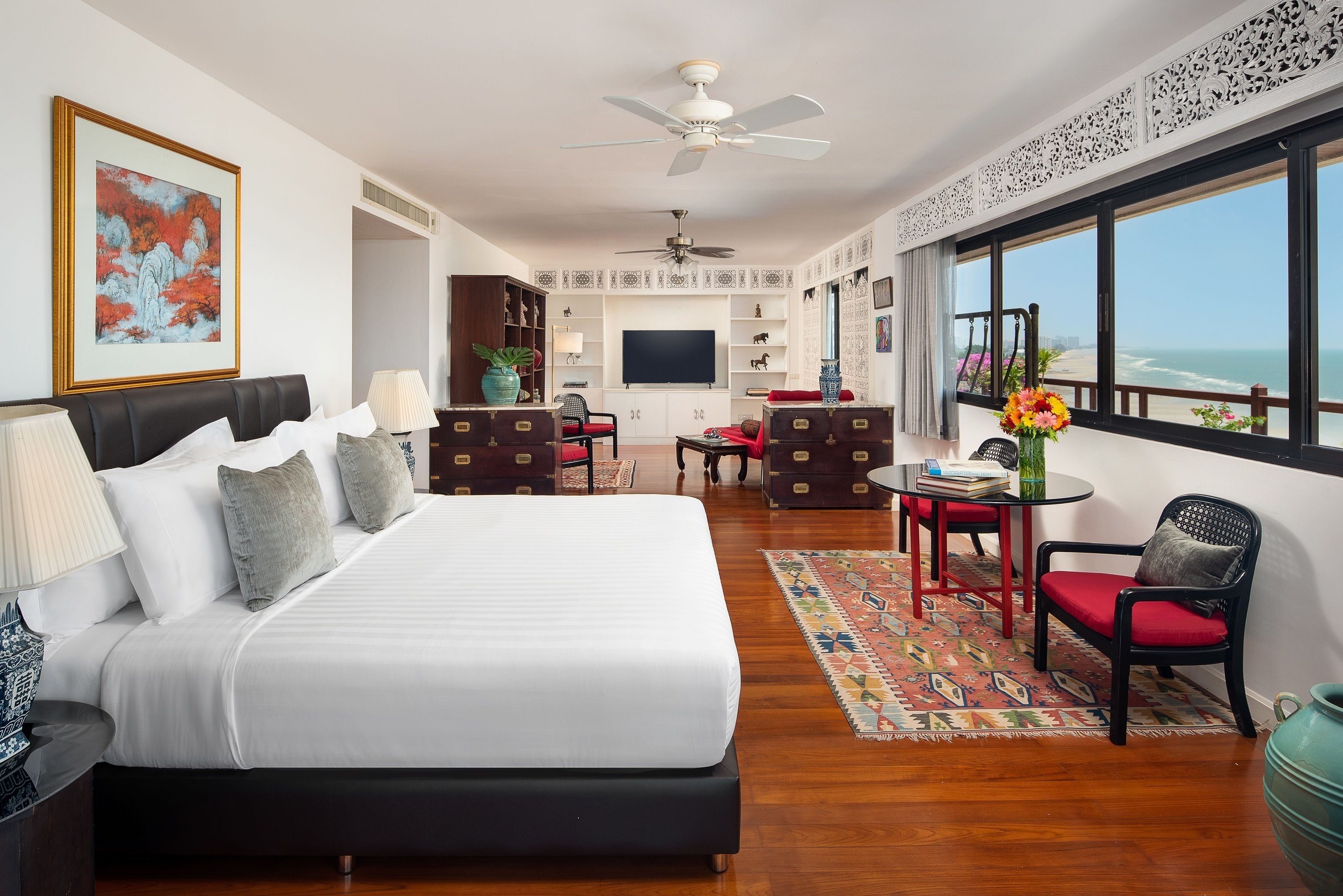 Een hotelkamer met een groot bed, een bureau met stoel, een televisie en uitzicht op zee.