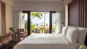 A hotel room with a large bed, a small table with chairs, a view of the sea, and a balcony with outdoor furniture.