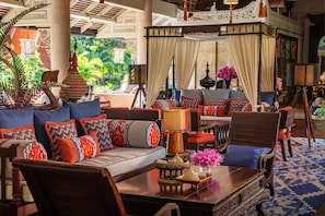 A spacious, elegantly decorated lounge area with a large sofa set, wooden furniture, and a view of lush greenery outside.