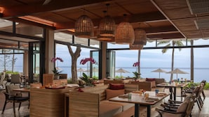 A modern outdoor seating area with wicker furniture, large windows, and a view of the sea.