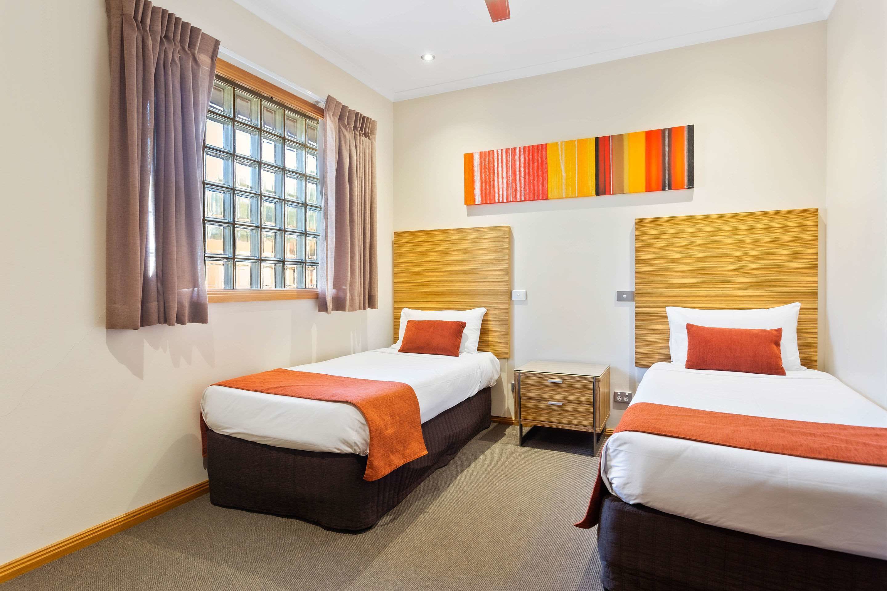 A hotel room with two beds, a window with curtains, a bedside table, and a modern abstract painting on the wall.