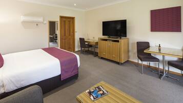 A hotel room with a bed, a desk, a TV, and a magazine on the coffee table.