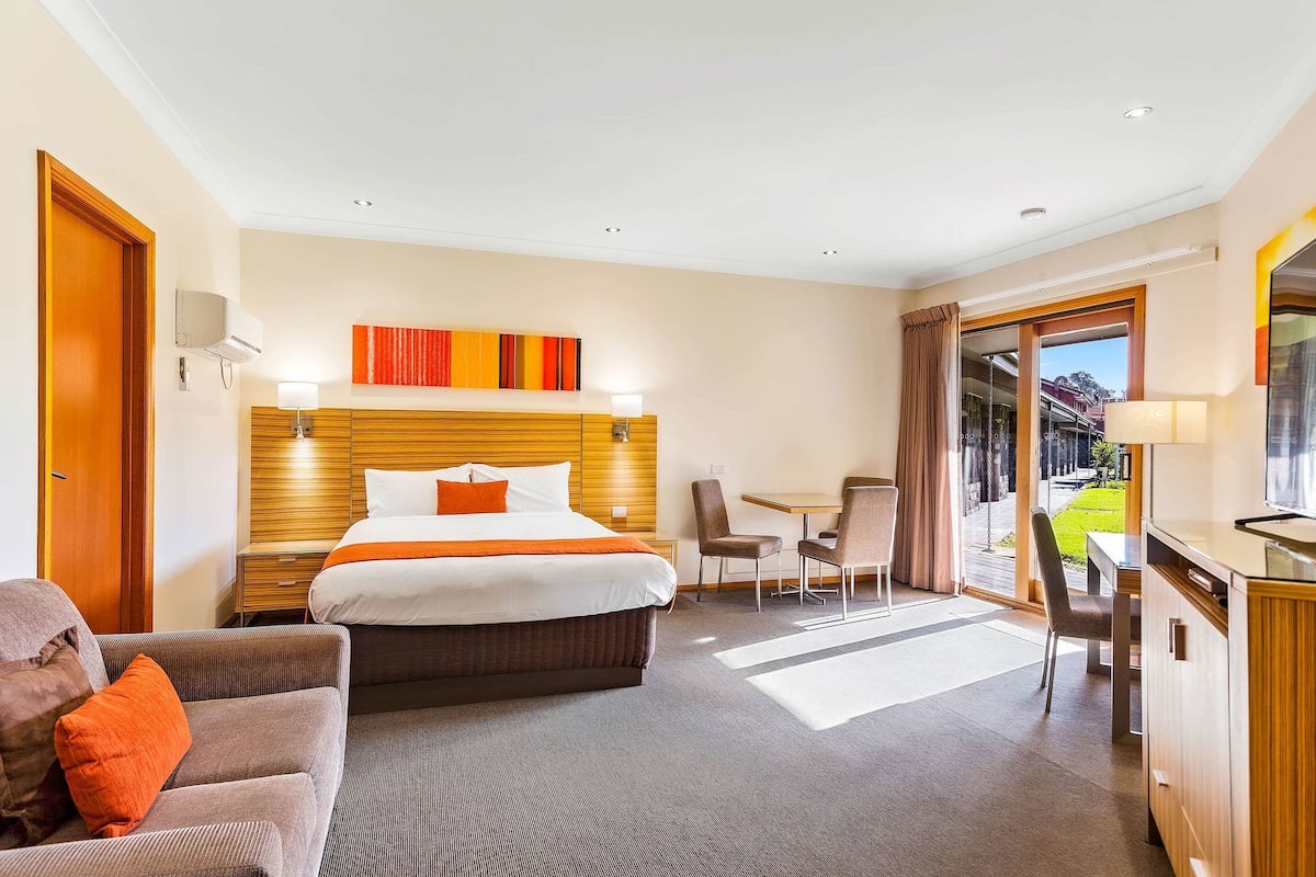 A hotel room with a large bed, a desk, a chair, and a small table.