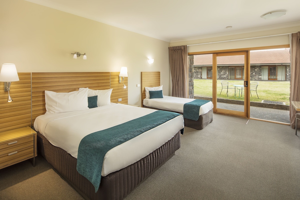 A hotel room with two beds, a large window, and a view of the courtyard.