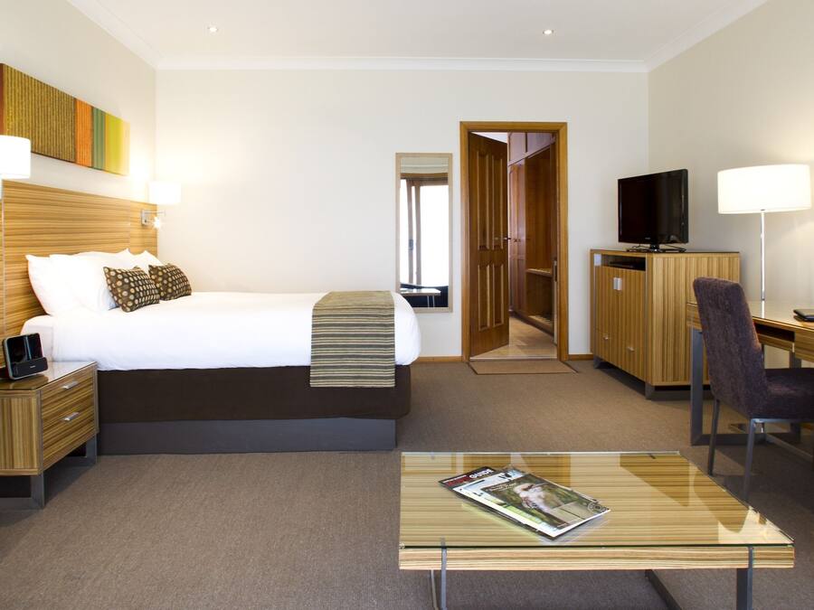 Een hotelkamer met een bed, nachtkastjes, een bureau met stoel, een televisie en een glazen salontafel.