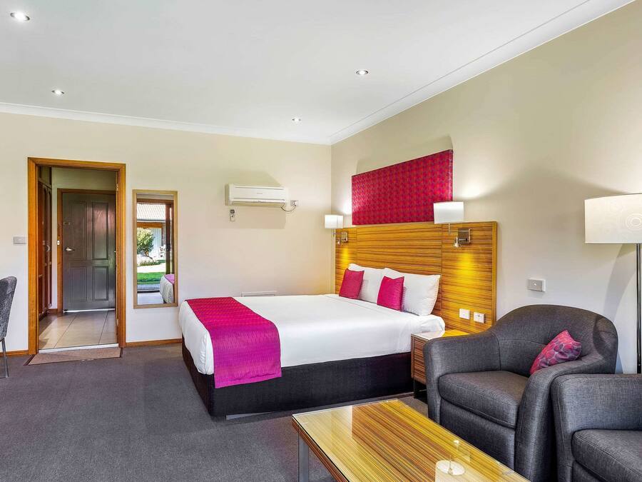 A hotel room with a bed, a desk, a chair, and a lamp.