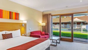 A hotel room with a large bed, a red armchair, a glass coffee table, and a view of a pool and outdoor area. - Julie-Anna Inn, Bendigo (Bendigo)