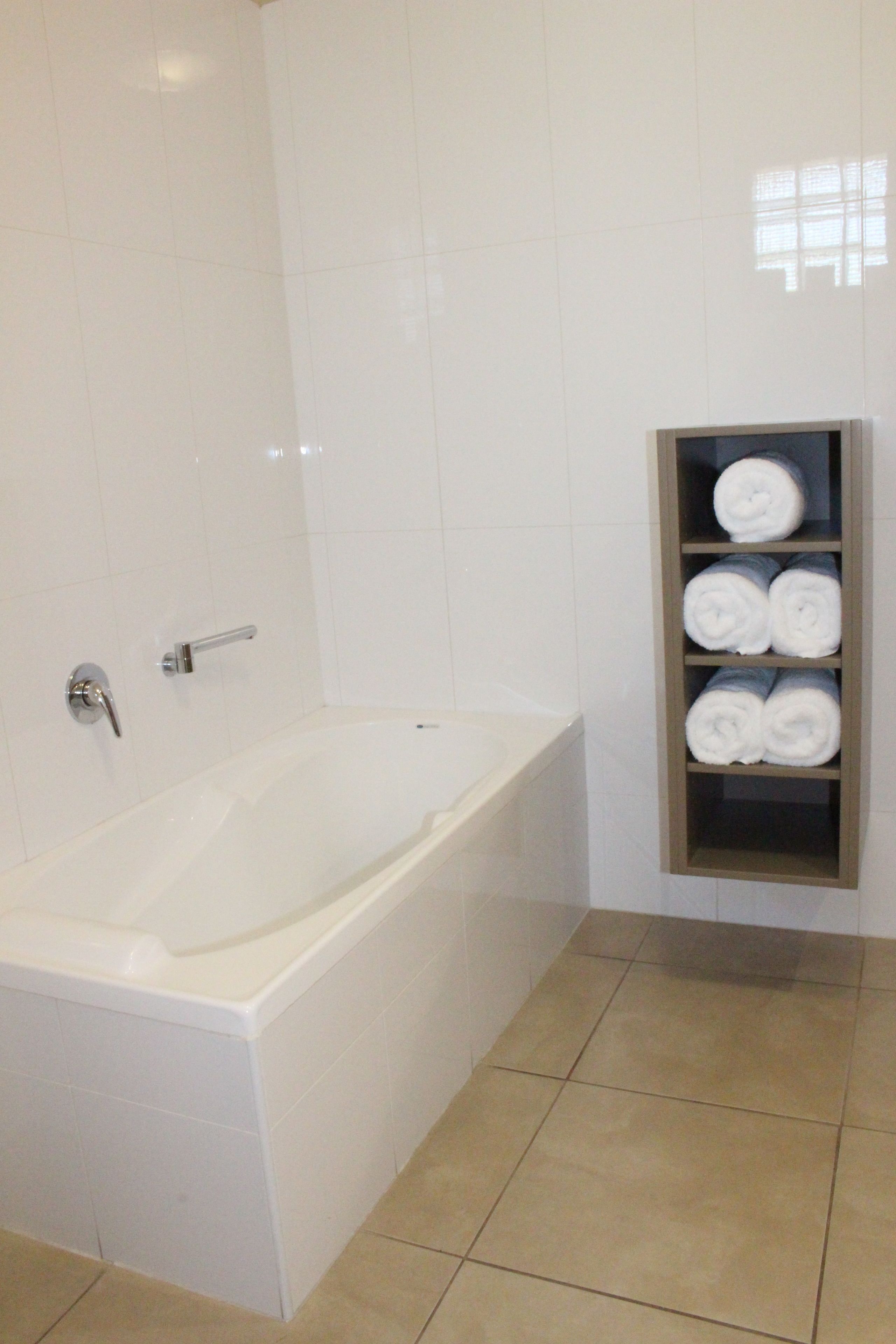 Une salle de bain avec une baignoire blanche, un porte-serviettes où sont soigneusement pliées les serviettes, et un sol carrelé.