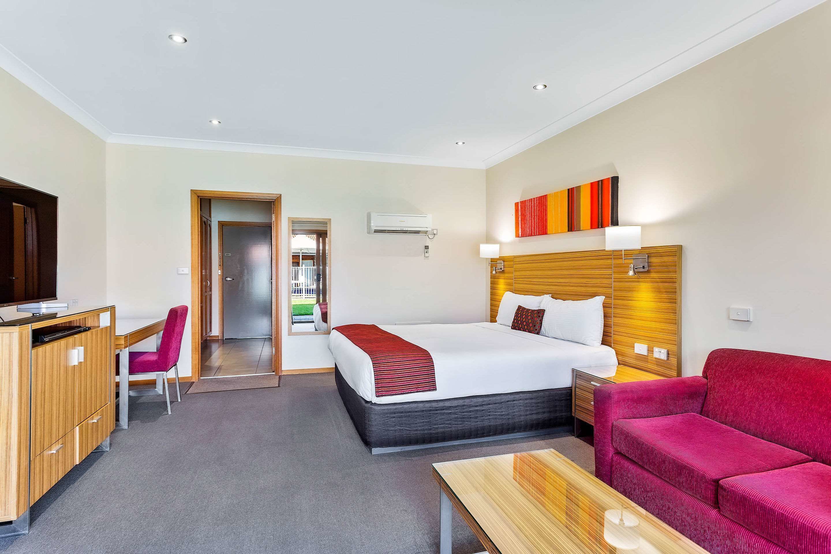 A hotel room with a bed, a desk, a chair, a sofa, and a TV.