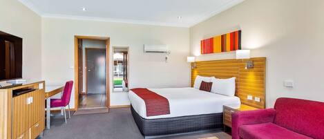 A hotel room with a bed, a desk, a chair, a sofa, and a TV.