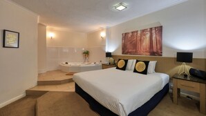 Habitación de hotel con una cama grande, zona de estar con escritorio y sillón, bañera y un cuadro en la pared.