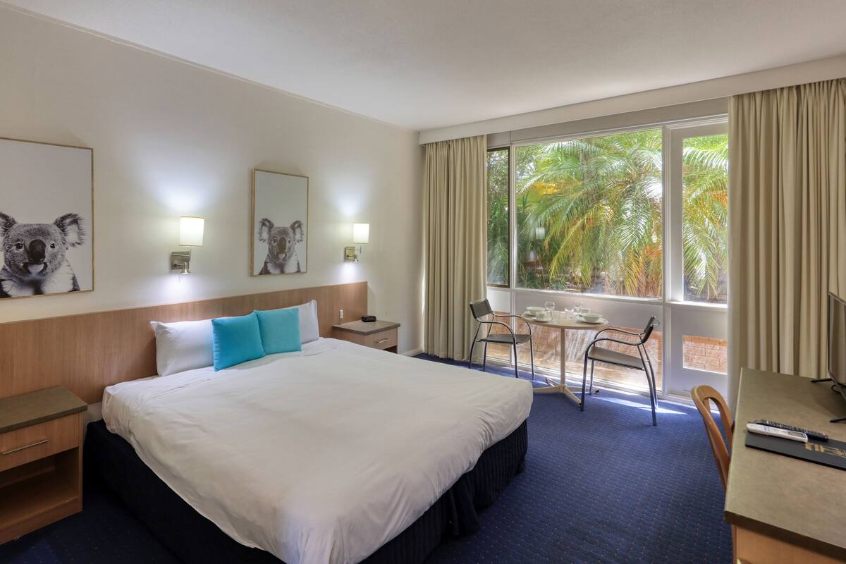 A hotel room with a bed, a desk, a chair, a TV, and a window with curtains.