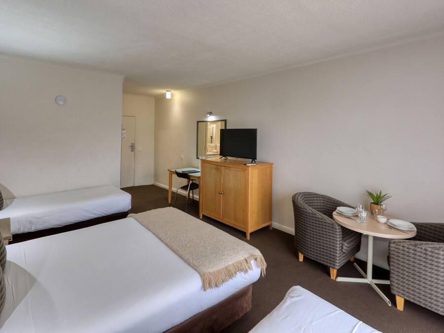 Una habitación de hotel con dos camas, un escritorio, un armario, un televisor y una pequeña mesa de comedor con sillas.