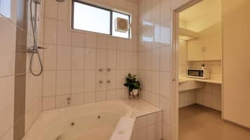 A modern bathroom with a bathtub, a shower, a window, and a small sink area with a microwave.