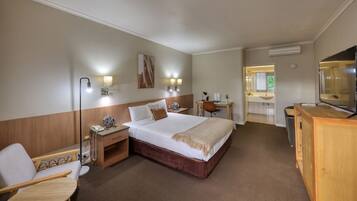 Een hotelkamer met een groot bed, nachtkastje, lamp, stoel, bureau en televisie.