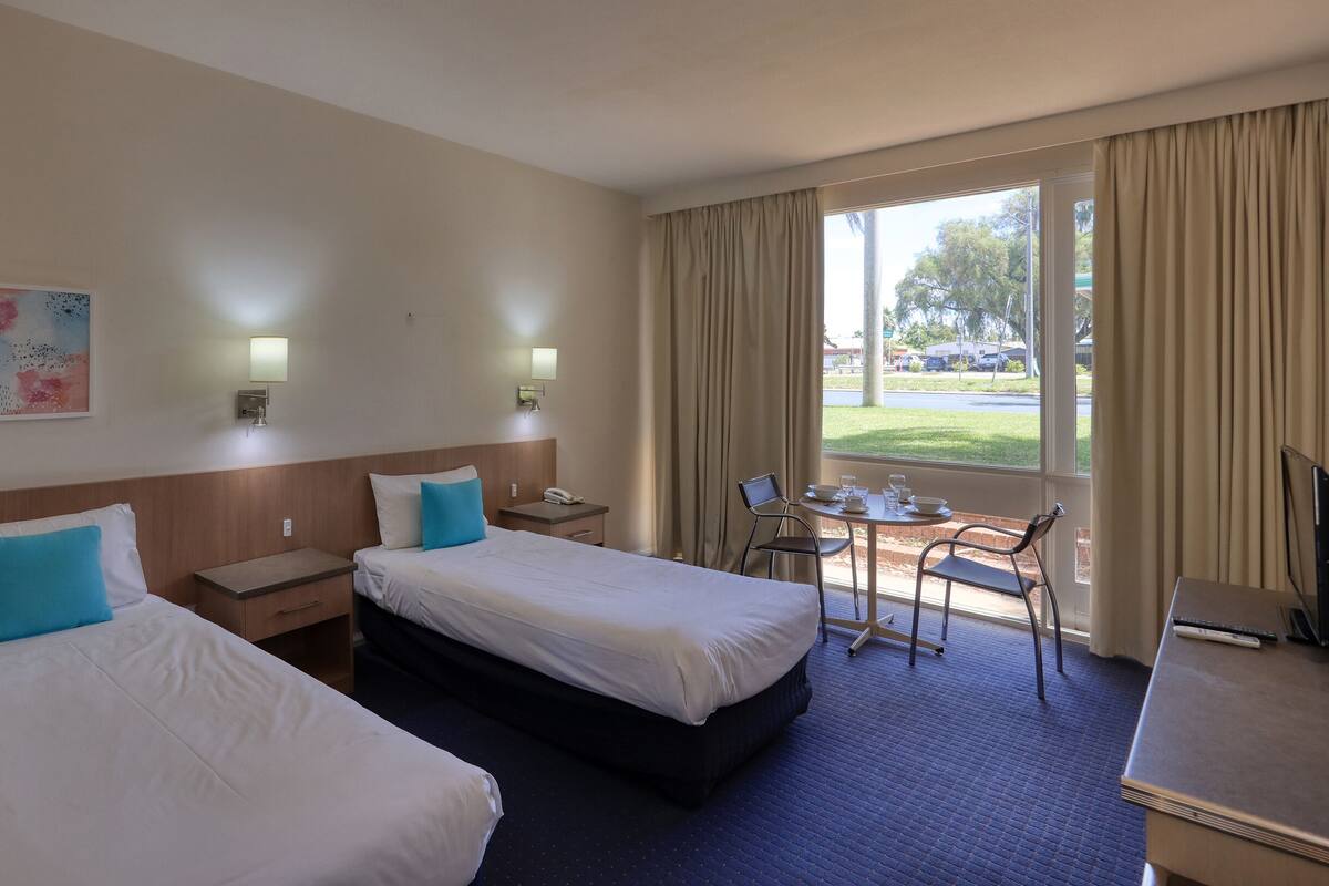 A hotel room with two beds, a desk, a chair, and a window with curtains.