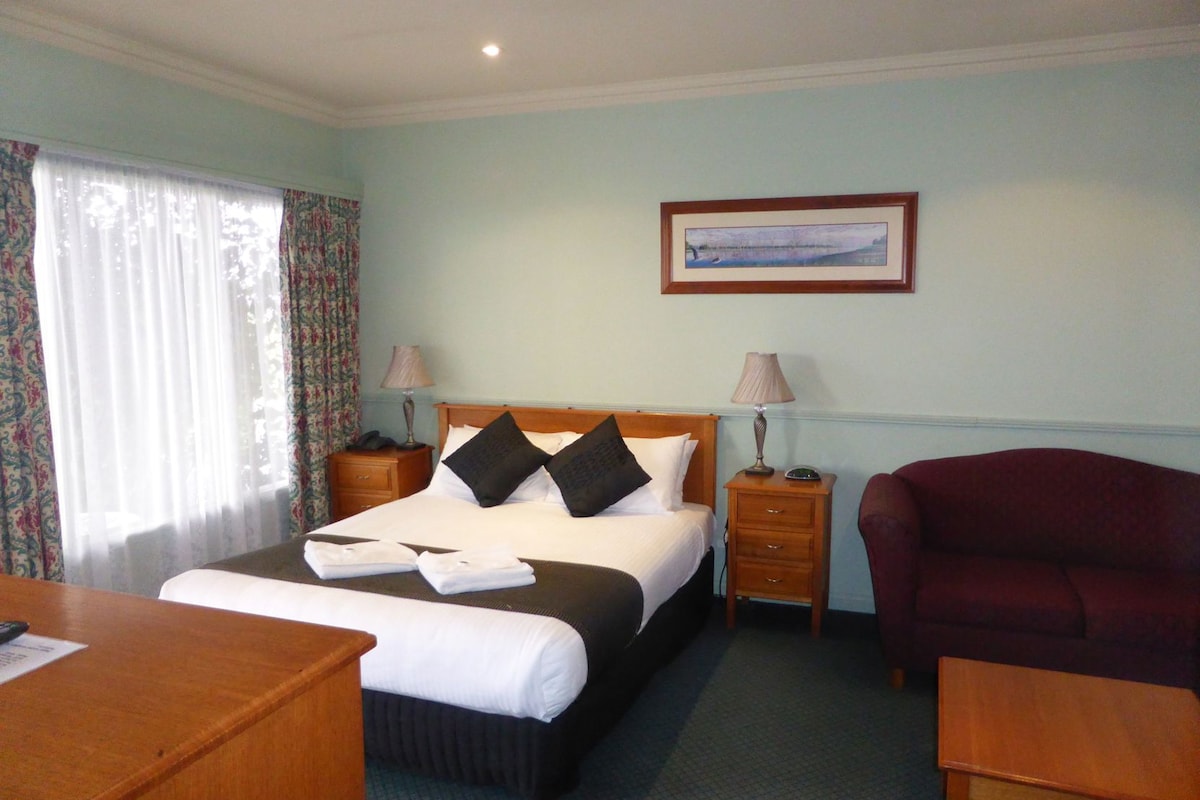 A hotel room with a bed, bedside tables, a desk, a chair, and a framed picture on the wall.