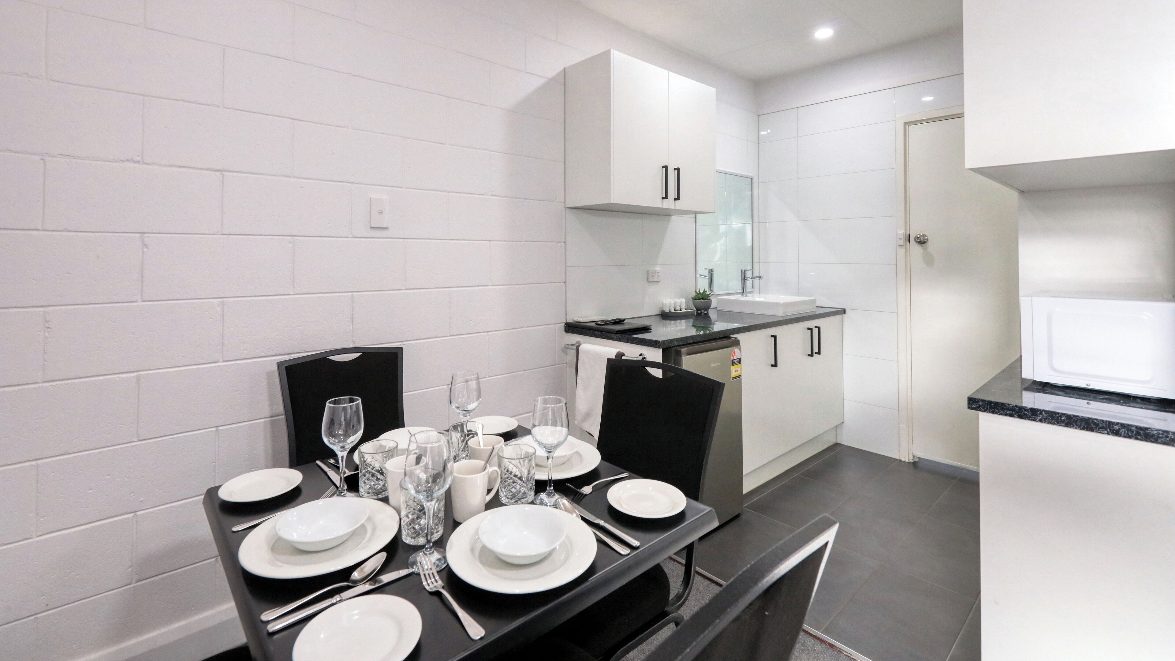 A modern kitchen with white cabinets, a black countertop, and a dining area set for four with plates, glasses, and cutlery.