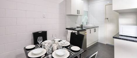 Una cocina moderna con armarios blancos, encimera negra y una zona de comedor preparada para cuatro personas, con platos, vasos y cubiertos.