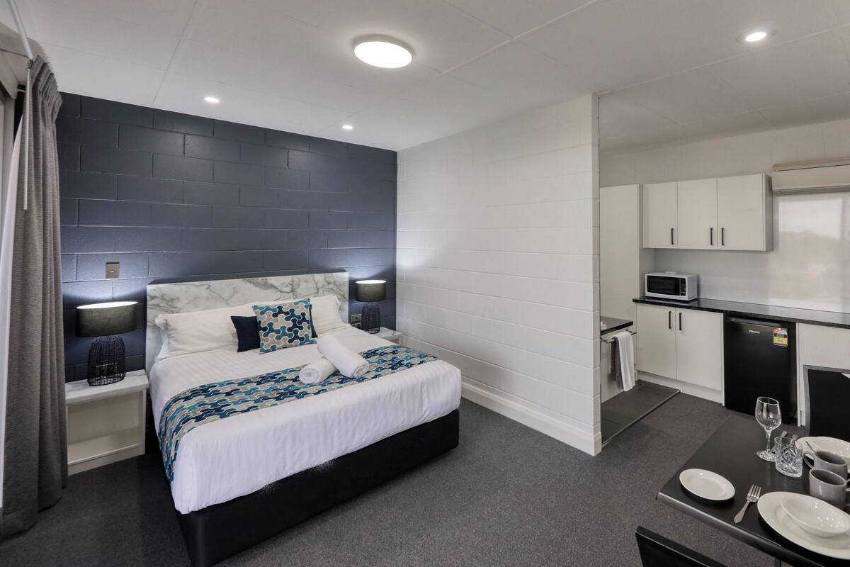 Une chambre d’hôtel moderne équipée d’un lit, de tables de chevet, d’une petite kitchenette et d’un coin repas.