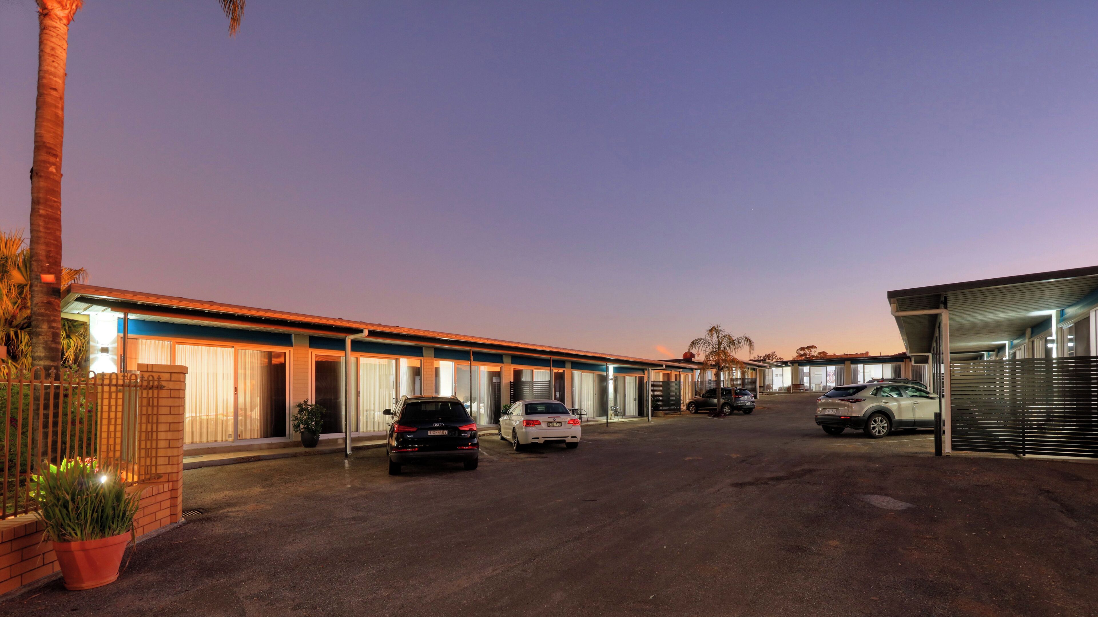 A hotel with a row of rooms, a parking area, and a covered walkway.