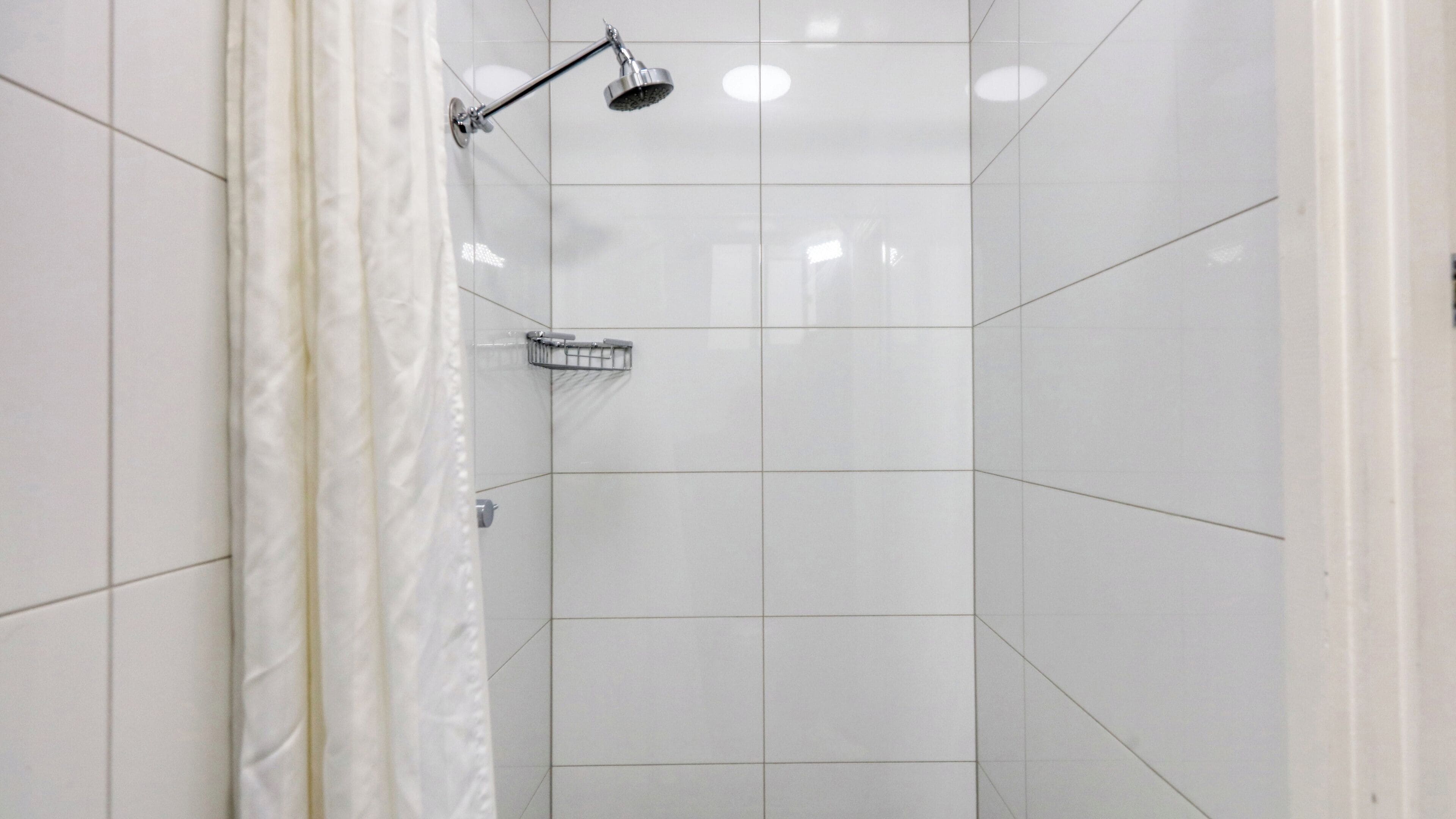 A shower area with white tiles, a showerhead, and a shower caddy.
