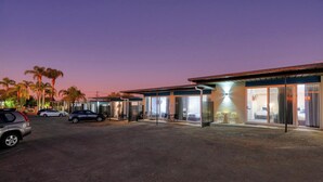 A hotel with a modern design, featuring a covered outdoor seating area with chairs and a table, and a large sliding glass door entrance. - Hilltop Motel (Broken Hill)