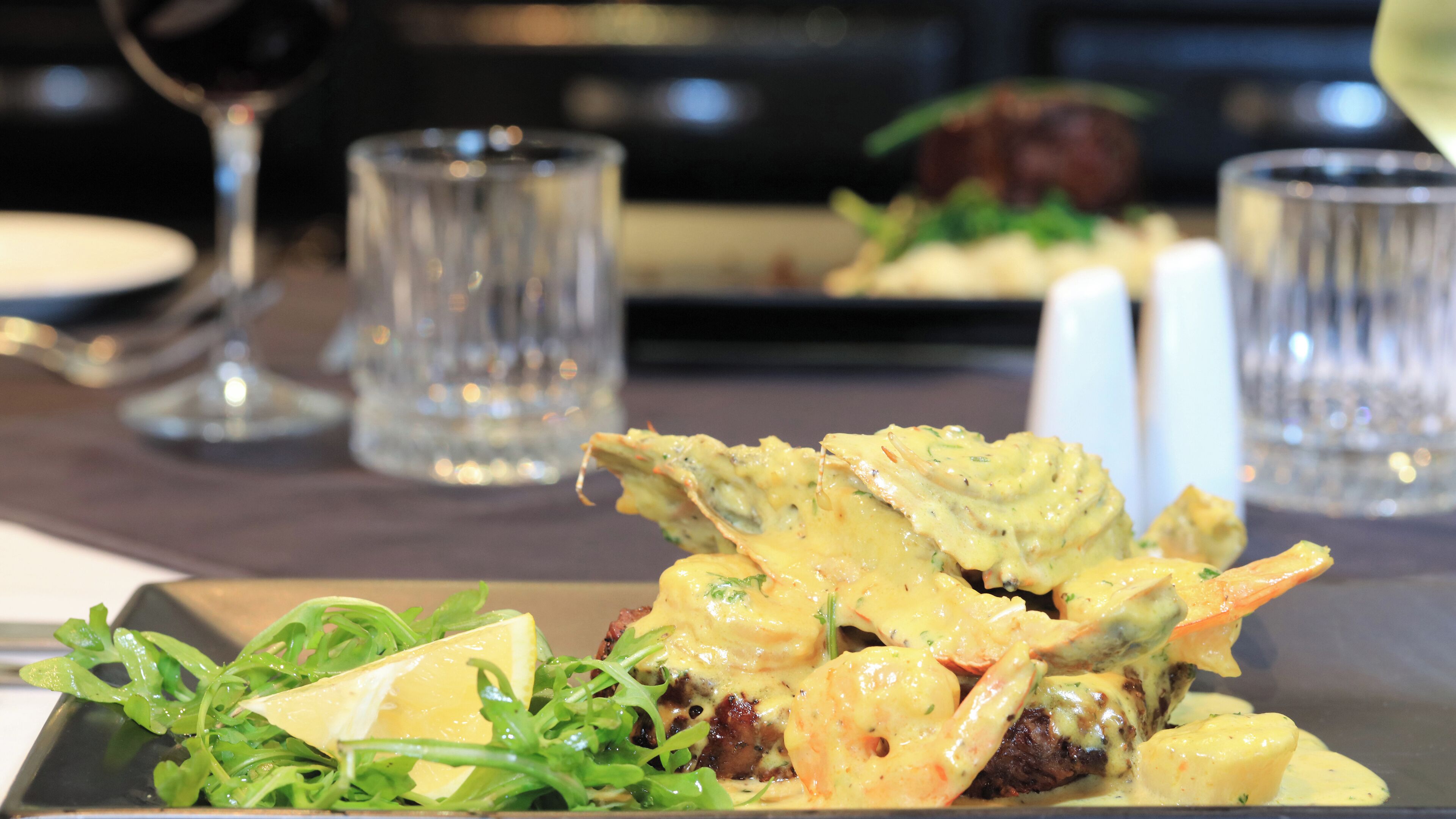 Une assiette garnie de légumes verts et nappée d’une sauce crémeuse, accompagnée d’un verre de vin blanc et d’un verre d’eau, le tout posé sur une table.