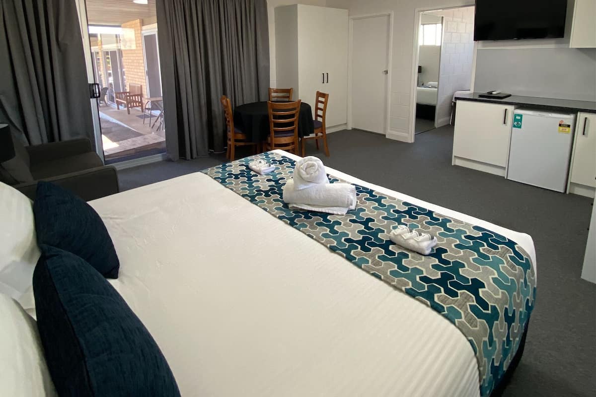Une chambre d’hôtel avec un grand lit, un bureau, une chaise, une télévision et une kitchenette.