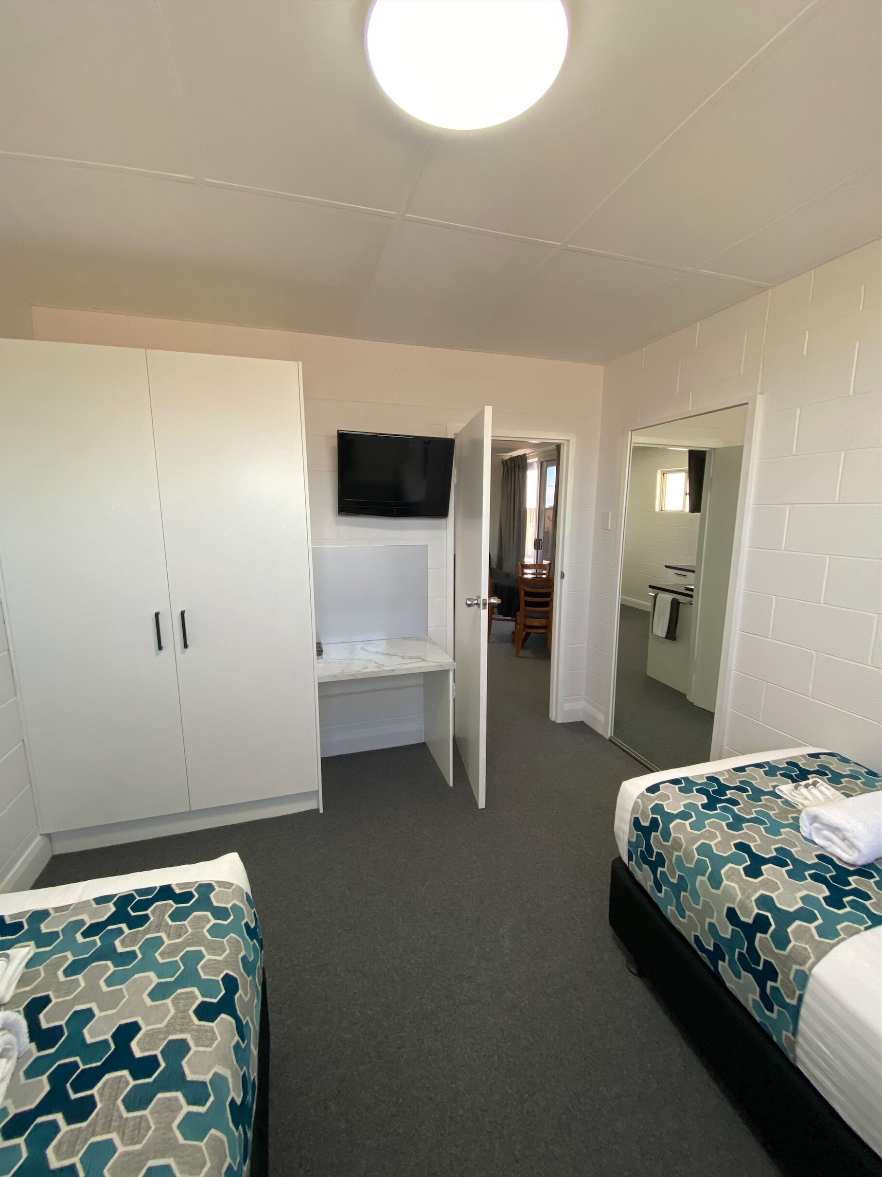 Hotelkamer met twee bedden, een aan de muur bevestigde televisie, een garderobe en een badkamer zichtbaar door een geopende deur.