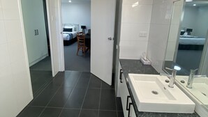 A modern bathroom with a large sink, mirror, and dark tiled floor. - Hilltop Motel (Broken Hill)