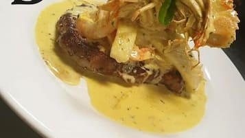 Een bord eten met vlees, garnalen en groenten, geserveerd op een wit bord.
