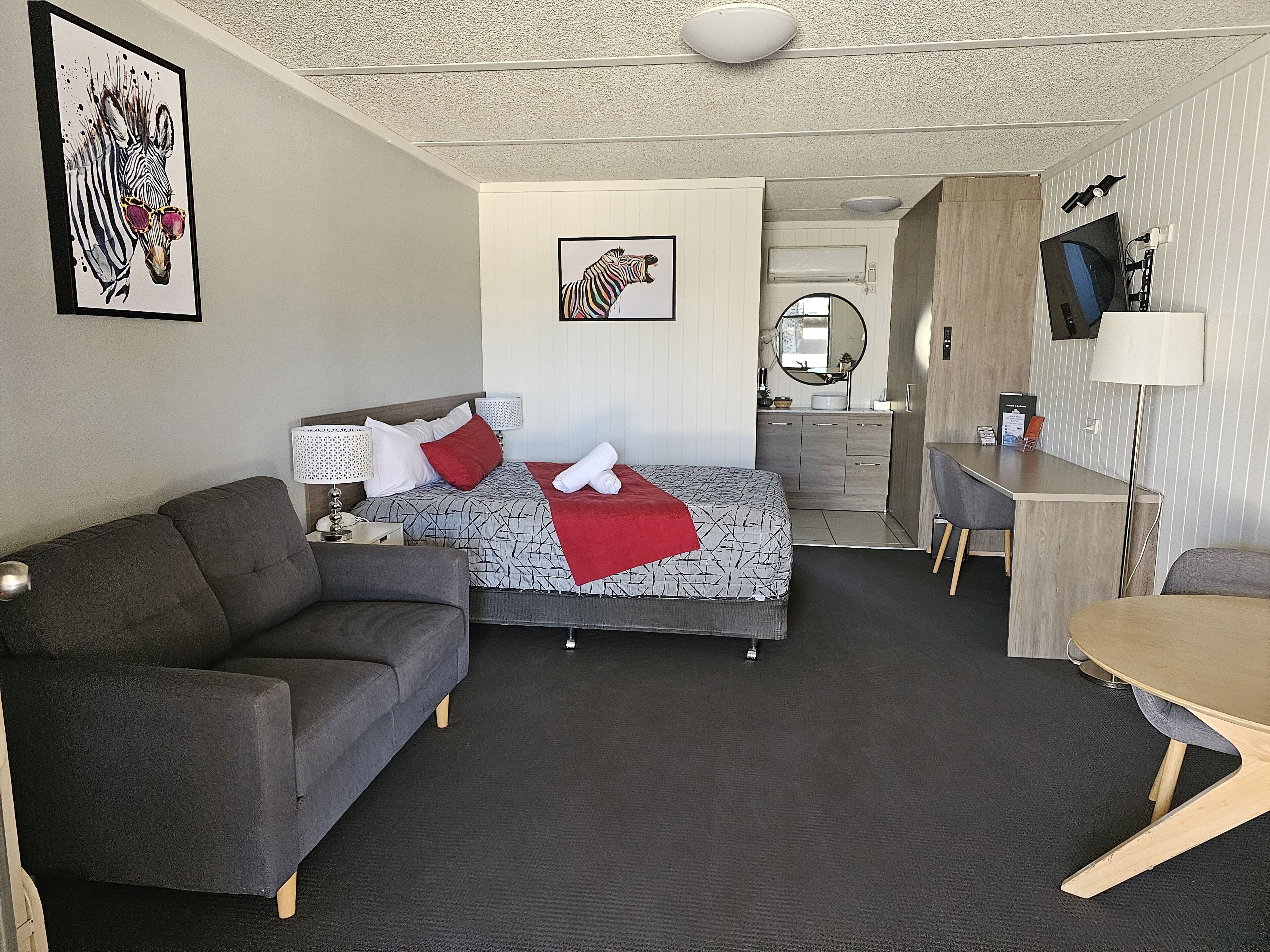 A modern hotel room with a bed, a sofa, a desk, and a TV.