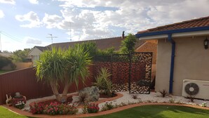 A well-maintained garden with a variety of plants and flowers, a decorative fence, and a lawn in front of a building with a tiled roof. - Cameo Inn Motel (West Wyalong)