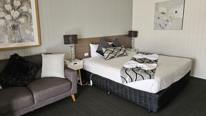A neatly arranged hotel room with a bed, bedside tables, a couch, and artwork on the walls. - Cameo Inn Motel (West Wyalong)