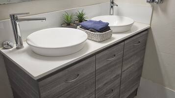 A modern bathroom with two sinks, a mirror, a hairdryer, and a small plant.