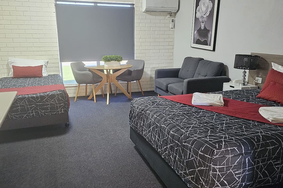 Ett modernt hotellrum med en stor säng, en soffa, ett matbord med stolar och ett litet bord med en växt.